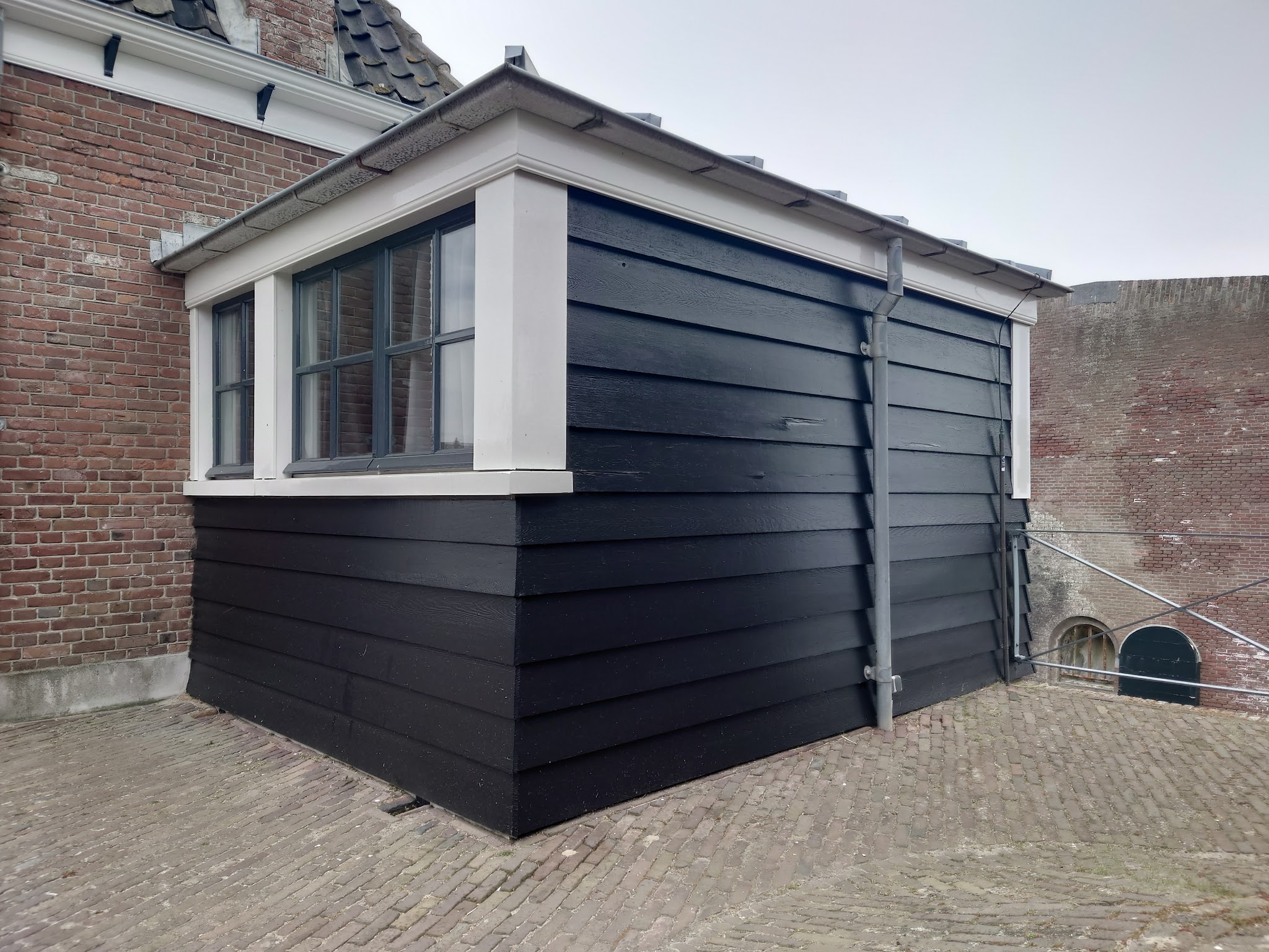 Zwart geschilderde houten aanbouw met witte kozijnen