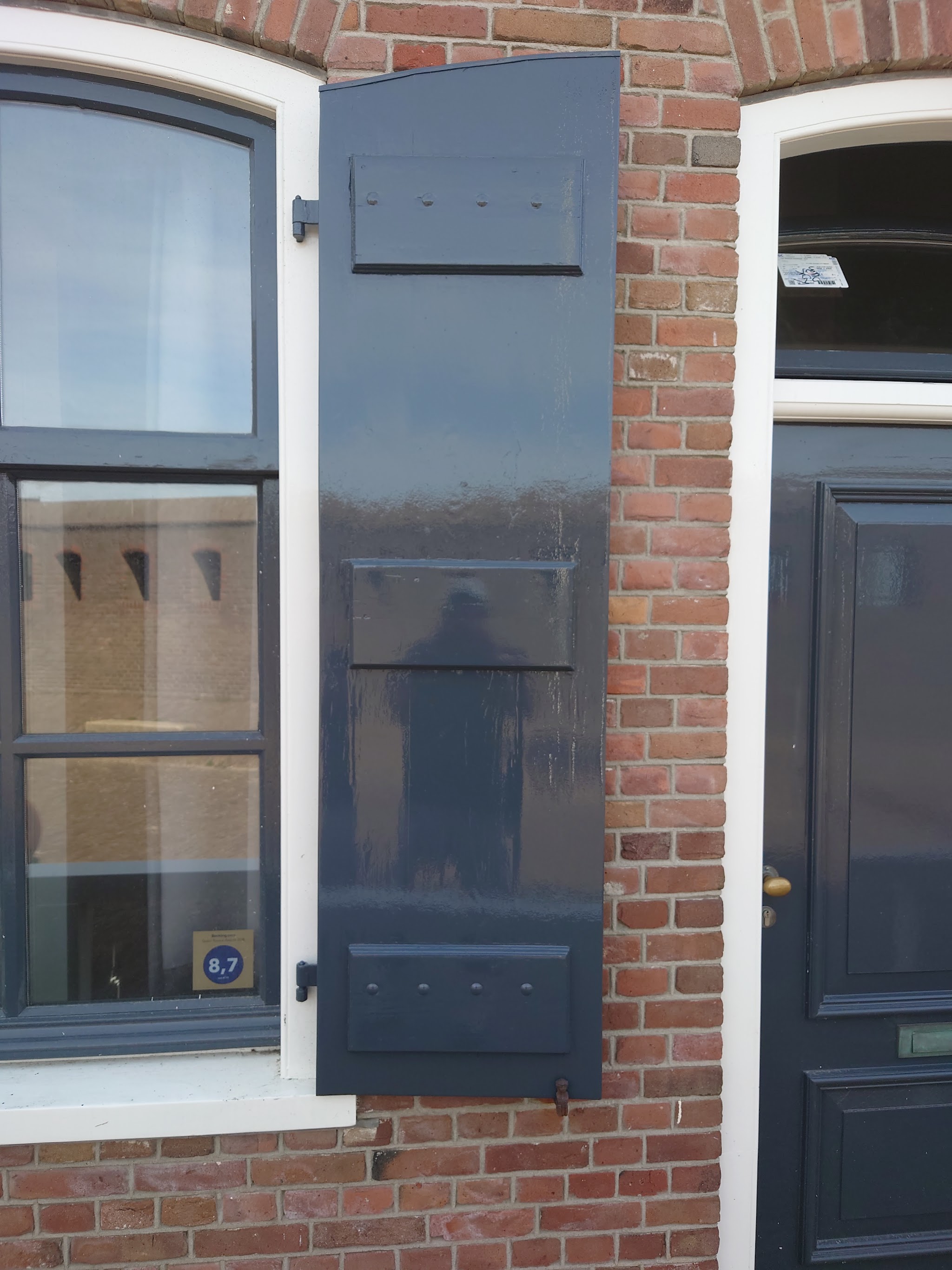 Donker geschilderd luik en voordeur met witte kozijnen in een bakstenen gevel