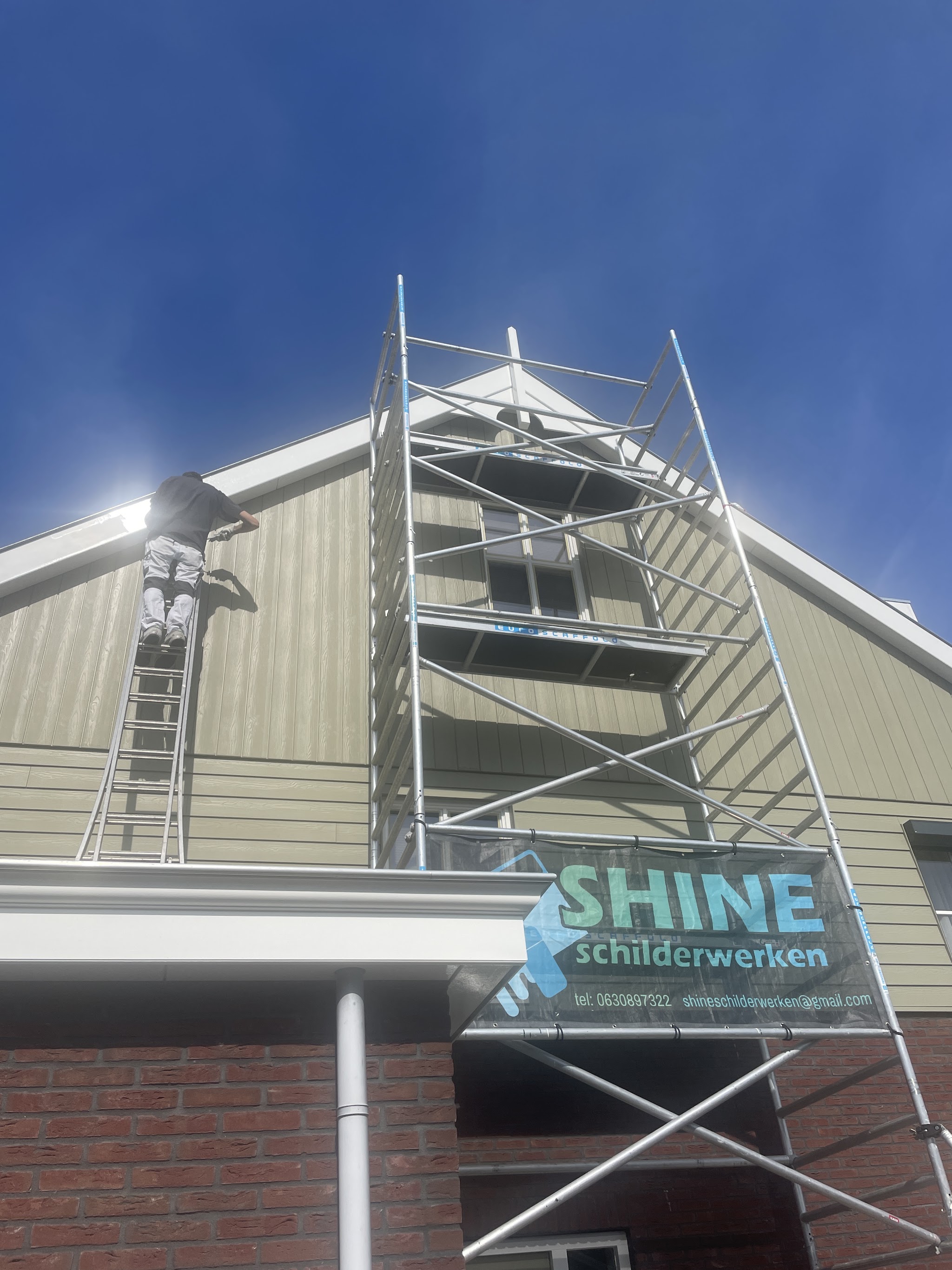 Schilder aan het werk op een rolsteiger met het Shine schilderwerken spandoek