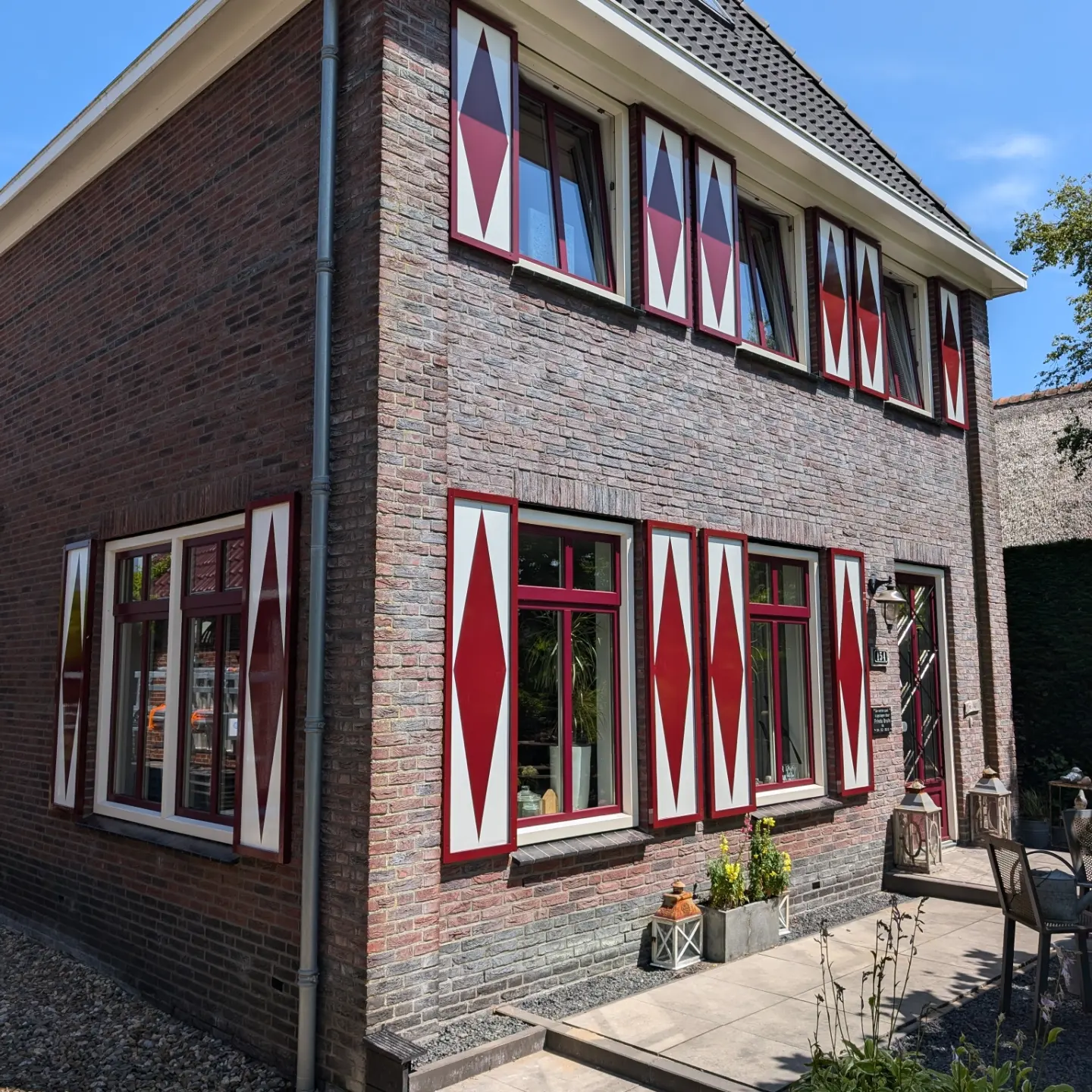 Bakstenen woning met rood-wit geschilderde luiken en rode kozijnen